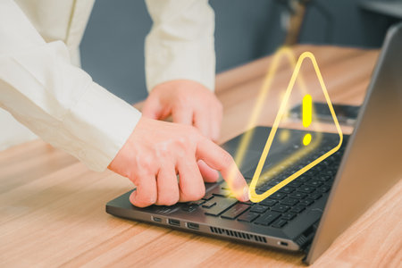 Adult man using computer laptop with triangle caution warning sign for notification error. Computer virus detected, personal data protection, network security and maintenance concept.の写真素材