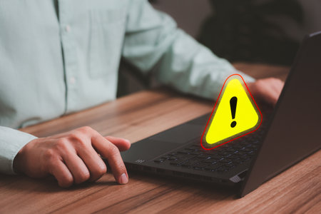 Adult man using a computer laptop with triangle caution warning sign for notification error. Concept technology of computer virus detected, personal data protection, network security and maintenance.の写真素材