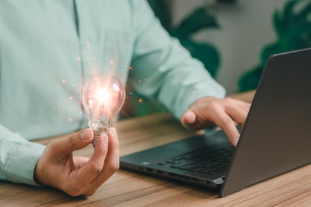 Man holding a light bulb while working on the computer to think and create new ideas with technological innovations and creativity Ideas inspired by online technology, innovation.の写真素材