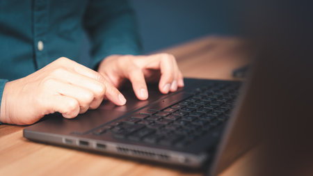 Close-up shot of young man working and typing on laptop computer keyboard on wooden table in cafe. Chat with AI or artificial intelligence using an artificial intelligence chatbot developed.の写真素材