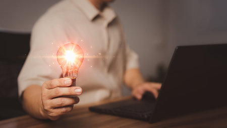 Adult man holding a light bulb while working on a computer laptop to think and generate new ideas...