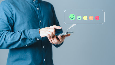 Client hands using a mobile phone with pop up smile face icon for feedback review satisfaction service opinion and testimonial. Customer service experience assessment and business satisfaction survey.の写真素材
