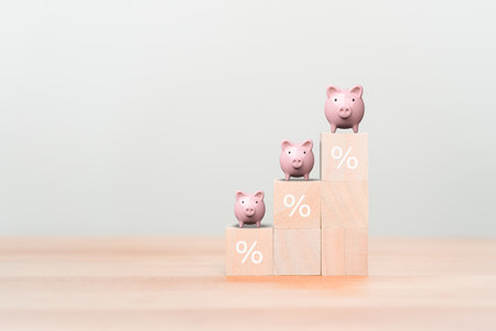 Piggy bank on wooden cube blocks with percentage sign on the table. Business, saving, investment, money, financial growth, interest rate increase, inflation, high price and tax rise concept.の写真素材