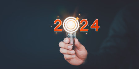 Businessman holding a light bulb with goal icon and the year 2024. 2024 business planning and strategy innovative business vision and new year resolution target, save energy efficiency concept.の写真素材