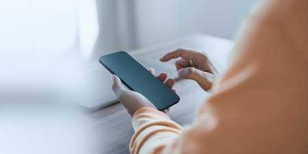 Young man holding and using a smartphone with blank desktop screen while working and drinking coffee in cafe. Mockup mobile phone.の写真素材