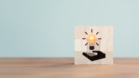 Wooden cube block with hand holding illuminated light bulb icon. Concept of new ideas with innovation, creative idea, new business plan, motivation, innovation, inspiration. Energy saving light bulb.の写真素材
