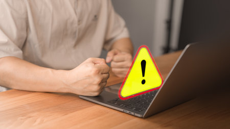 Young man using a computer laptop with triangle caution warning sign for notification error. Concept technology of computer virus detected, personal data protection, network security and maintenance.の写真素材