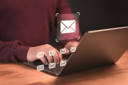 Concept of Email marketing, send e-mail or news letter, online working internet network. Male hand using a computer laptop typing on keyboard and surfing the internet on office table with email icon.の写真素材