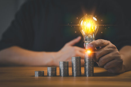 Adult man hand holding a light bulb putting on money stack. New ideas for savings money, taxes, retirement, working, small business, finance, investment, financial planning, and financial concept.の写真素材
