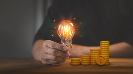 Man hand holding a light bulb and 3d money stack on table. New ideas for savings money, taxes, retirement, working, small business, finance, investment, financial planning, and financial concept.の写真素材