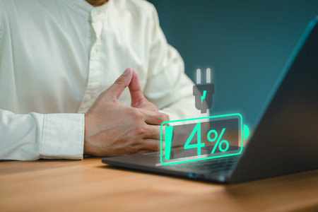 Close-up of a person seated at a desk with a laptop showing a low battery icon at 4%, symbolizing...