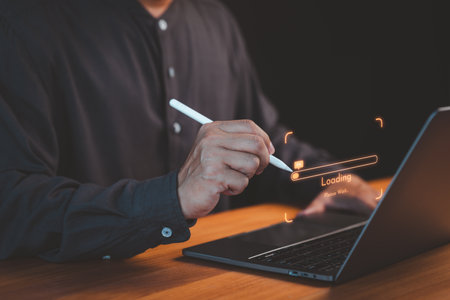 Close-up of a person using a pen with a laptop, highlighting a glowing loading bar and digital interface, representing technology, progress, and innovation.の写真素材