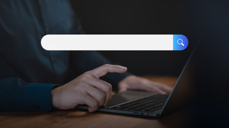 Adult man using a laptop searching on the internet. SEO technology networking, representing online browsing, information seeking, and digital search technology in a modern workspace.の写真素材