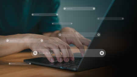 Focusing on a search bar with a magnifying glass icon. Concept of represents online searching, research, and digital information gathering. Male hand types on a laptop keyboard.の写真素材