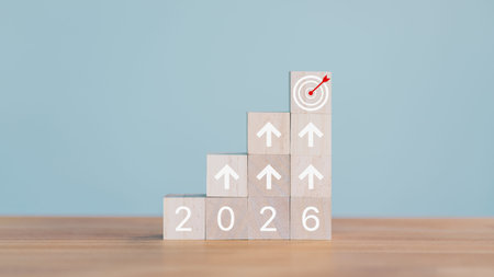 Wooden cube blocks stack to form a staircase with upward arrows and the year 2026 at the base. A...