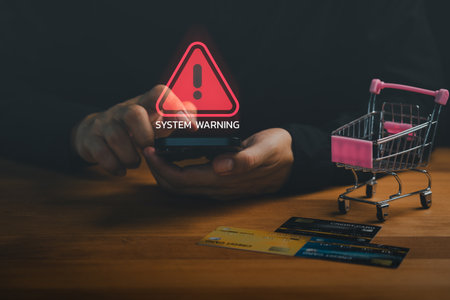 Customer using mobile phone with system warning icon, credit cards, and shopping cart symbolizing online fraud, cyber security risk, financial scam, payment danger and e-commerce security warning.の写真素材