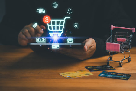 Customer using tablet with shopping cart icon, credit cards, and miniature trolley symbolizing online shopping, e-commerce, payment, retail, digital marketplace, delivery and modern technology.の写真素材