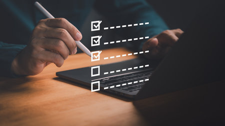 Person using a pen with a laptop to tick off items on a virtual checklist, symbolizing productivity, workflow, project planning and efficiency tools. Digital checklist and task management concept.の写真素材