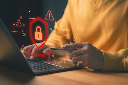 Person holding a credit card while using laptop, with red warning symbols and a digital padlock,...