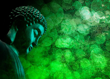Bronze Zen Buddha Statue Meditating with Blurred Textured Green Backgroundの写真素材