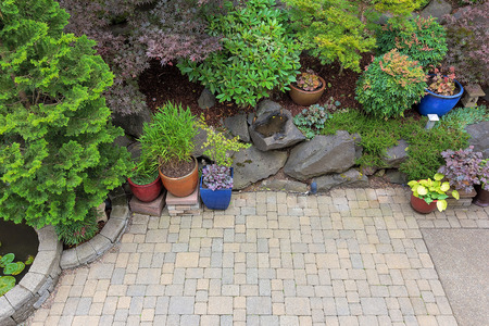 Backyard garden landscaping with paver bricks patio hardscape trees potted plants shrubs pond rocks and decor