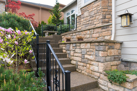 House front entry with concrete stairs iron rod railings stone wall planter siding by frontyard gardenの写真素材
