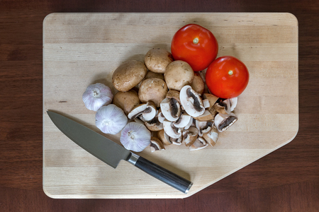 Mushrooms tomatoes garlic cloves vegetable with kitchen knife on wood cutting boardの写真素材