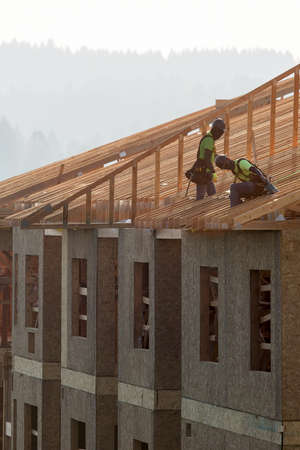 Roofing contractors working on framing the roof of new apartment building at construction siteの写真素材