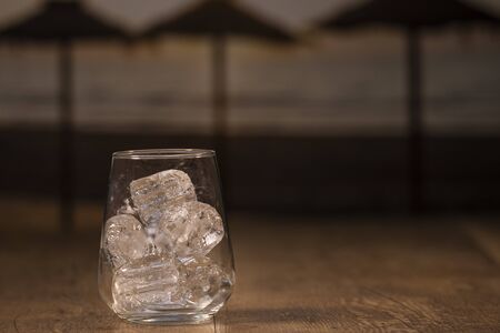 A sturdy glass cup with ice cubes on a wooden tableの写真素材