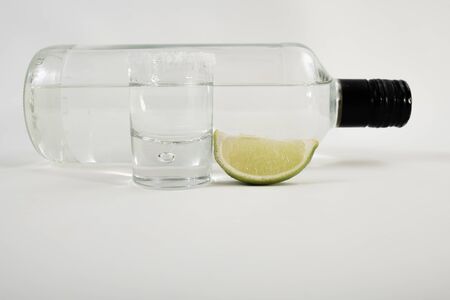 Detail of tequila served in a glass with a slice of lemon and a bottle of tequila isolated on a white background - Close-upの写真素材
