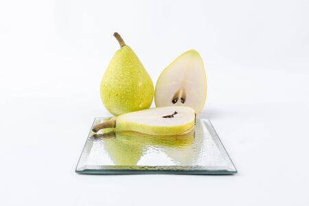 A delicious whole pear accompanied by slices of green pear on a glass plate insulated on a white background - Freshly harvested sweet pearsの写真素材