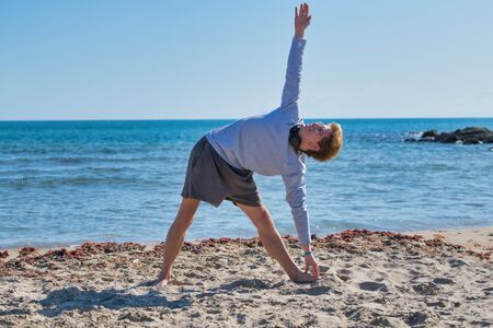Handsome boy on the shores of the beach with beautiful blue water stretching as he looks up smiling on a sunny day. Photo portrait.の写真素材