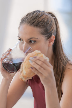Pretty girl drinking soda which is served in a glass cup which she holds with one of her hands while...