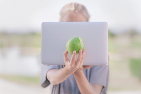 Pretty girl placing a green apple in front of a young green laptop that does not see her face since...