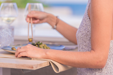 Hands of a girl whose face cannot be seen resting on a table where there are glasses of wine and a...