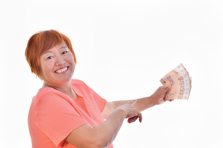 Asian woman smiling with 50 euro banknotes in one hand and with the other pointing, isolated on white background. Commercial exchange concept.の写真素材