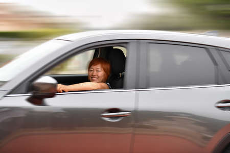 Smiling asian woman looking at the camera while driving a fast gray car, travel concept. Defocused and distorted background.の写真素材