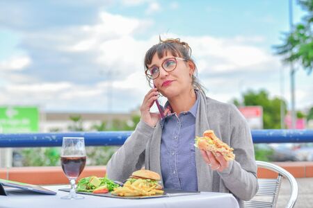 Woman eating hamburgers and talking on mobile phoneの写真素材