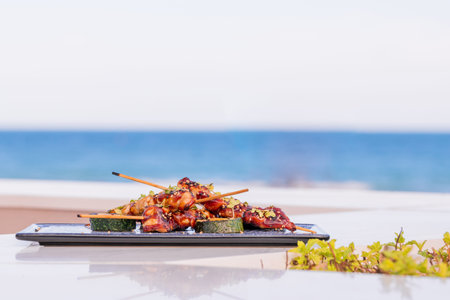 Succulent roasted vegetables served with skewers on small black food chopping board placed on table...