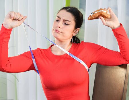 Woman looks concerned at a measuring tapeの写真素材