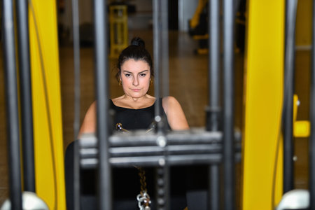 Focused looking woman uses a leg adductor machine at a gym with an out of focus foreground and...
