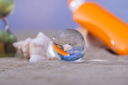 Close-up of a crystal ball in front of some out of focus seashells, a pair of sunglasses and an...