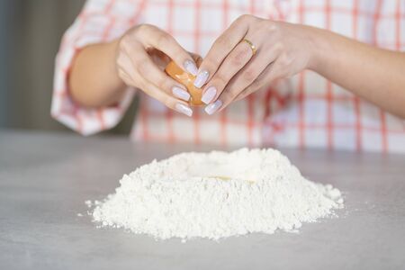 Close-up of a woman opening an egg to add it to a flour mound on a kitchen counter. Cooking concept.の写真素材