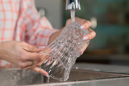 Woman rinsing a glass under a faucetの写真素材