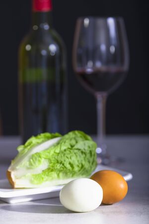 Close-up of a pair of hard boiled eggs, one of them peeled, with lettuce on a plate and an out of focus half full glass of wine and a bottle in the background. Healthy eating concept.の写真素材