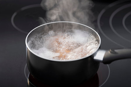Close-up of a saucepan on a glass ceramic cooktop filled with foamy boiling water. Cooking concept.