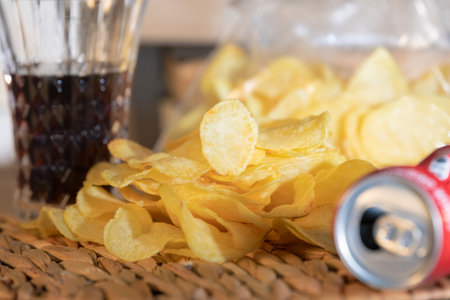 Close-up of a bunch of delicious looking potato chips surrounded by empty can and a glass