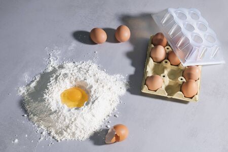 Egg in flour with eggshells and carton of eggsの写真素材