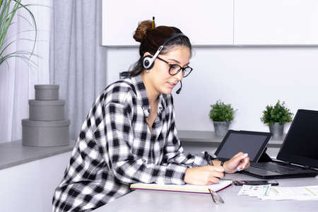view of a Young woman working from home office. operator using laptop and take notesの写真素材