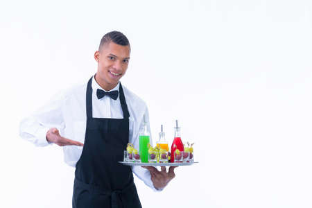 Handsome young waiter holding a tray with assorted liquor bottles and glass shots filled with grapes on a light background. Service and vegan cocktails concept.の写真素材
